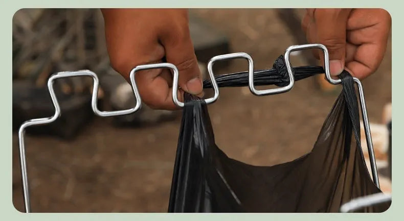 Silver folding stainless steel garbage bag holder bracket on a wooden surface.