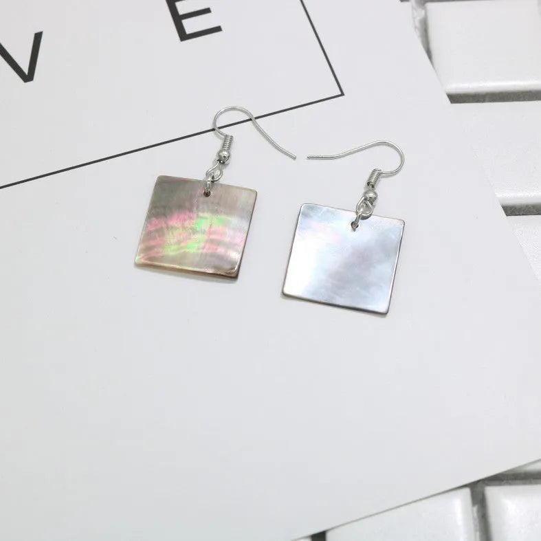 A pair of geometric shell earrings in a square panther design next to a rectangular shell design on a neutral background.
