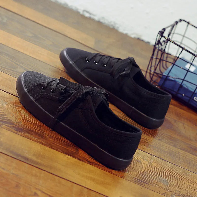 All-black low-top women's canvas shoes with flat rubber sole and lace-up front