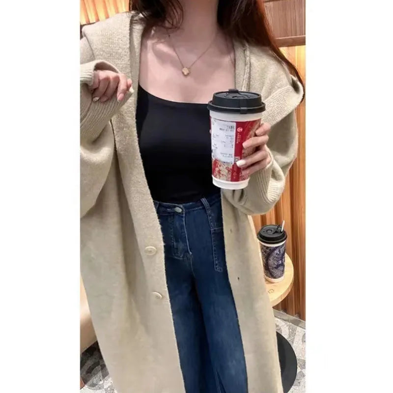 A woman wearing a long, beige, hooded knitted cardigan with a loose fit and below-the-knee length.