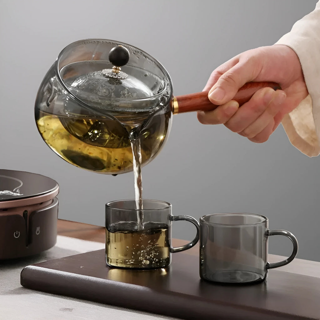 Transparent rotary glass teapot with wooden handle and built-in infuser on countertop