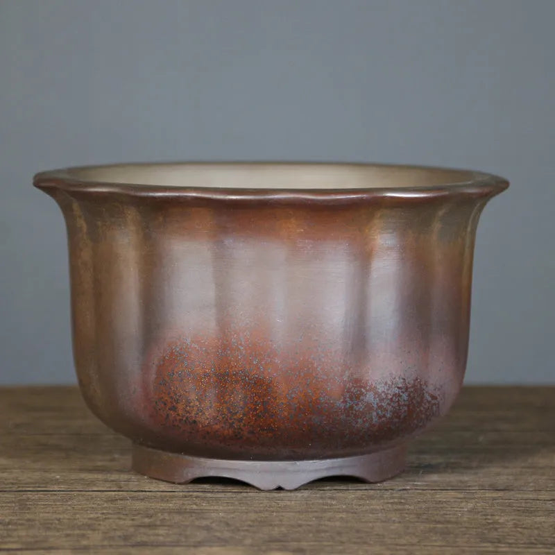 Indoor antique carved purple sand ceramic flowerpot in S1696 firewood colour on a wooden surface.
