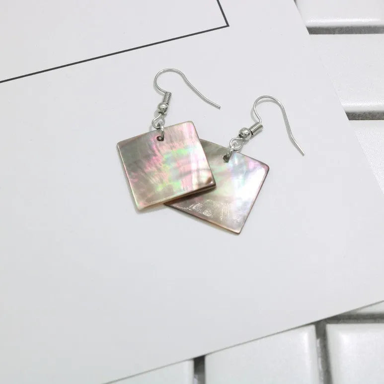 A pair of geometric shell earrings in a square panther design next to a rectangular shell design on a neutral background.