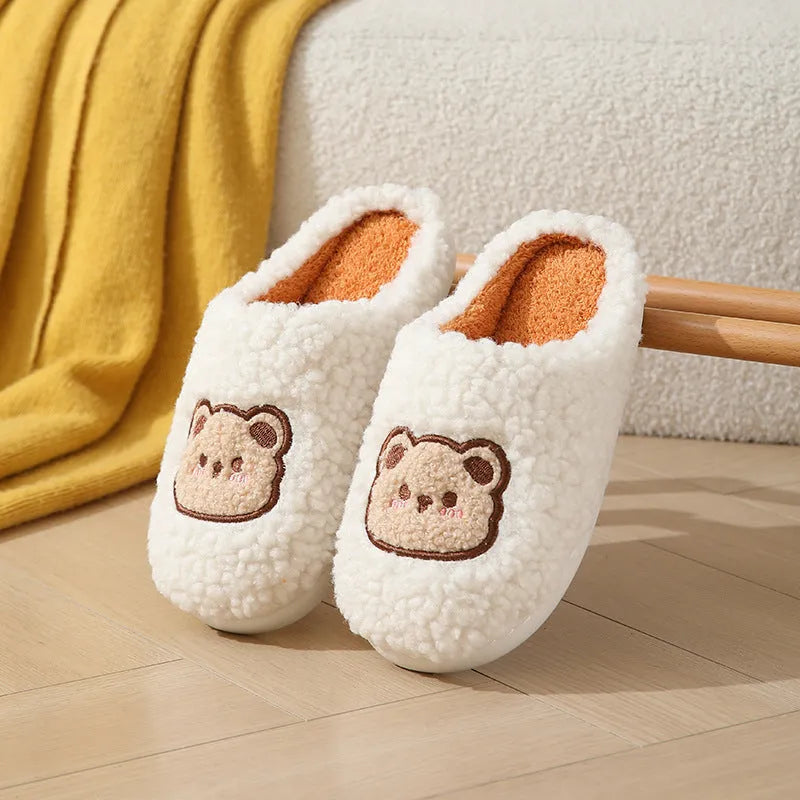 Pair of cute cartoon bear winter slippers with plush upper and non-slip TPR sole on a bedroom floor
