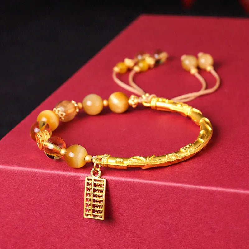 Close-up of a women's beaded bracelet with a diamond-shaped abacus tag bead, tigereye, citrine, and yellow tower crystal stones on copper.