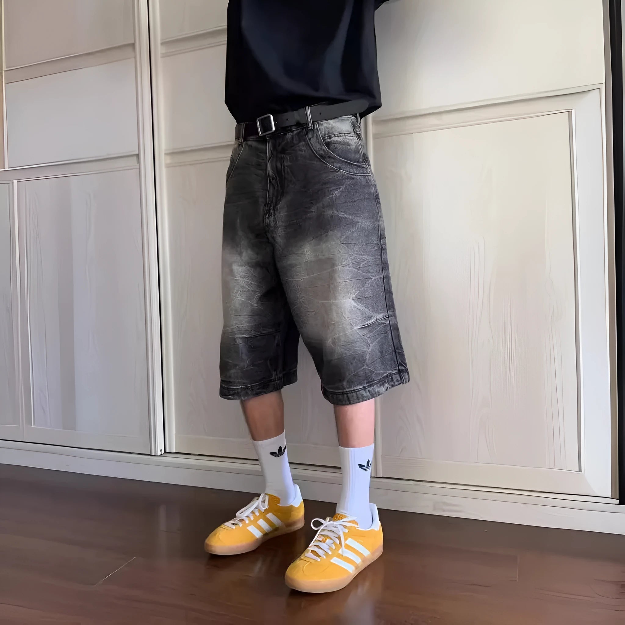 Man wearing loose straight-leg washed denim shorts in blue, showing cropped length and casual style.