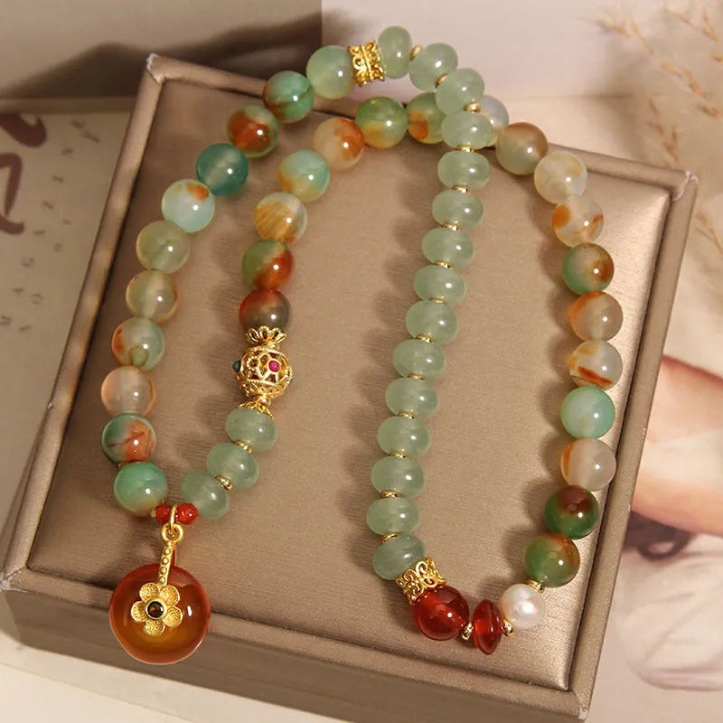 Gold-toned double ring chain bracelet with a peacock green agate safety buckle pendant and rhinestone details.