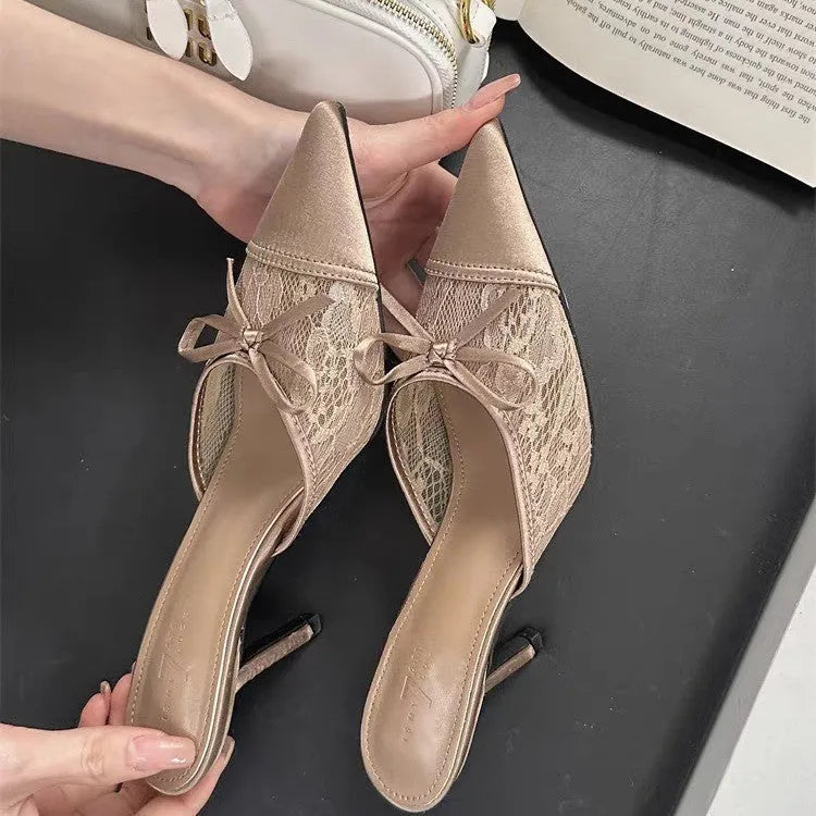 Women's light brown lace high heels with a pointed toe and a black bowknot detail on the front.