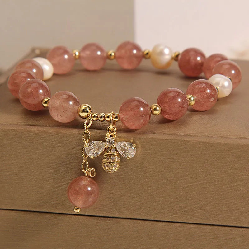 Close-up of a women's bracelet with pink strawberry quartz beads, white freshwater pearls, and sparkling zircon charms on an alloy chain.