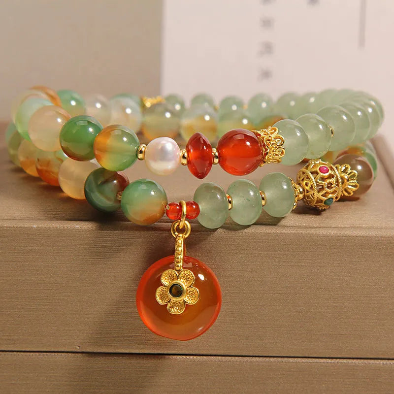 Gold-toned double ring chain bracelet with a peacock green agate safety buckle pendant and rhinestone details.