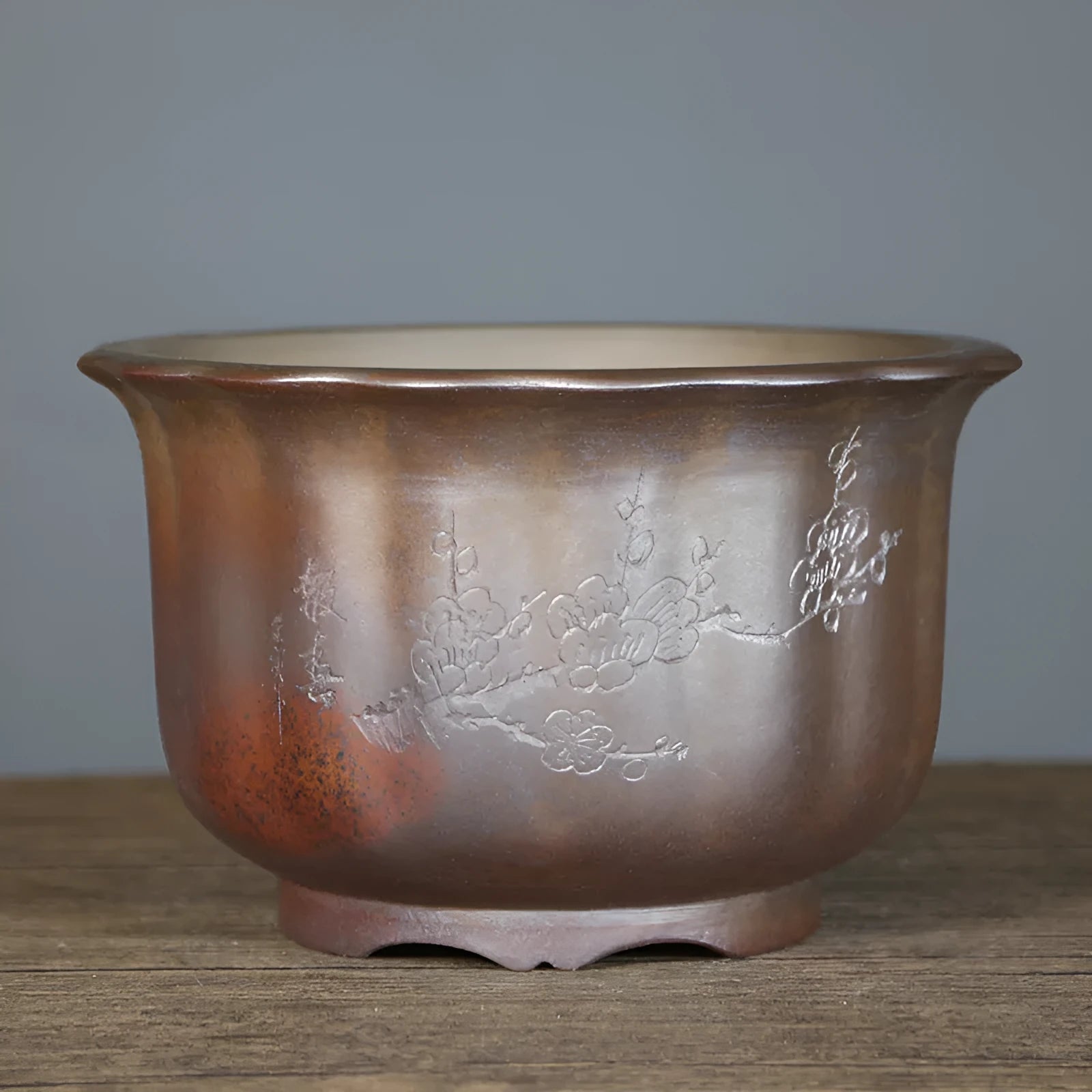 Indoor antique carved purple sand ceramic flowerpot in S1696 firewood colour on a wooden surface.