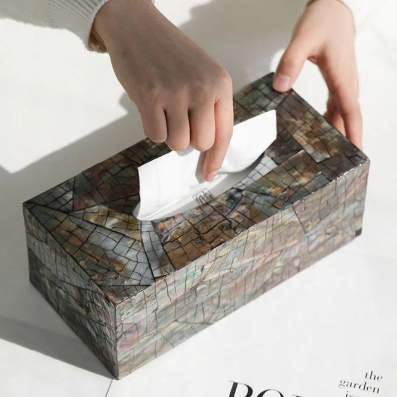 A black rectangular shell tissue box holder with a removable lid on a wooden coffee table.