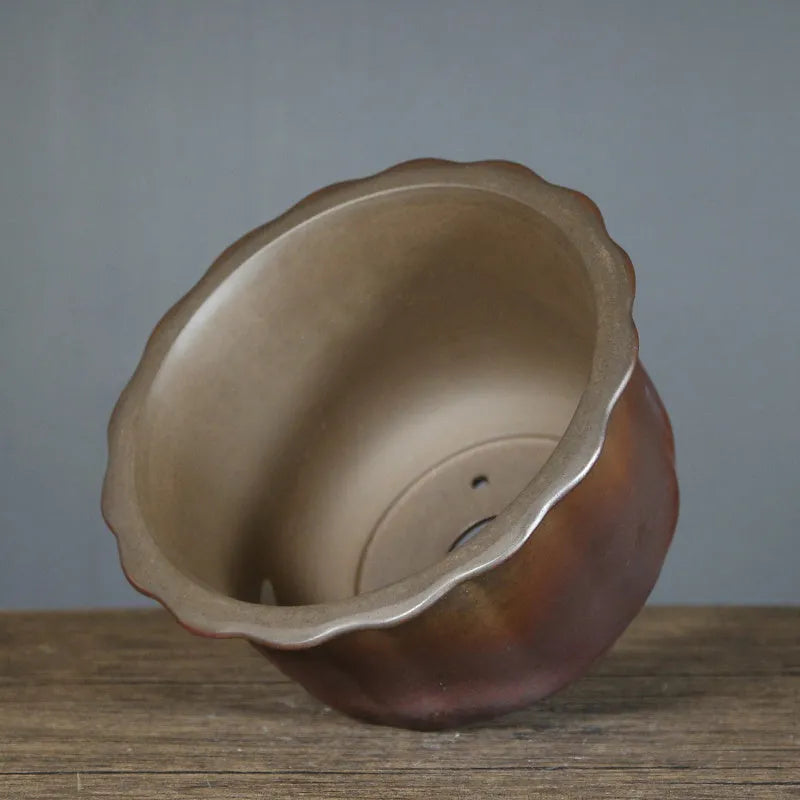 Indoor antique carved purple sand ceramic flowerpot in S1696 firewood colour on a wooden surface.