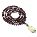 Close-up of a rosewood bead bracelet with 108 beads and a carved Hotian jade pendant.