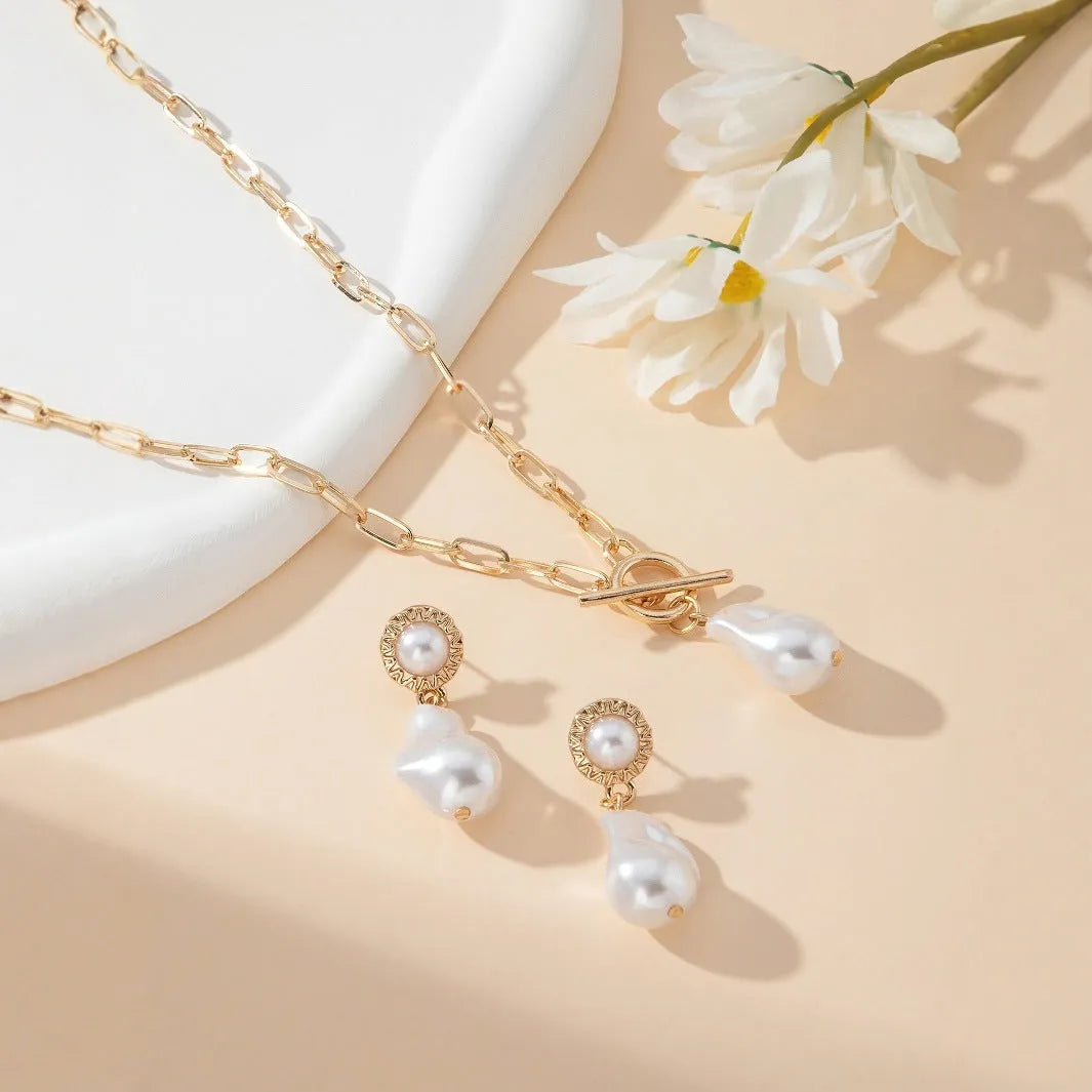 Gold tone retro style necklace and matching pearl ear studs set for women on a flat surface.