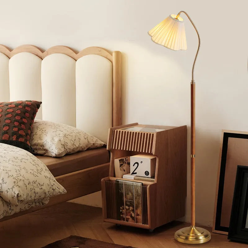 Solid wood floor lamp with fabric shade in walnut colour placed beside a sofa in a living room