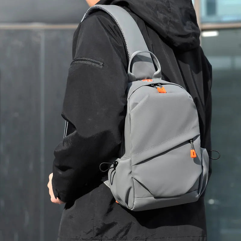 Men's black polyester crossbody bag with a single shoulder strap, shown in a casual setting.