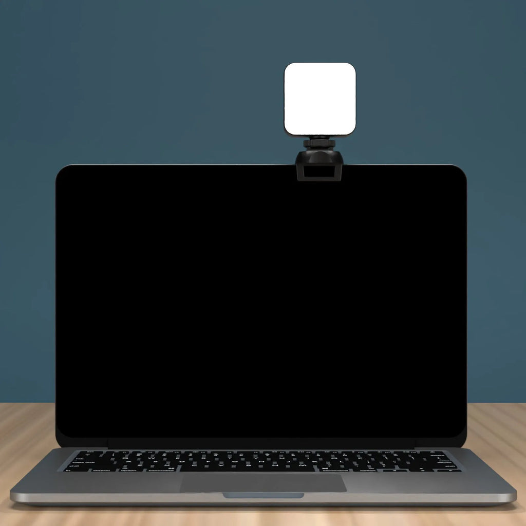 Silver 5600K LED video light cube clipped onto a laptop, with shelf and wire included