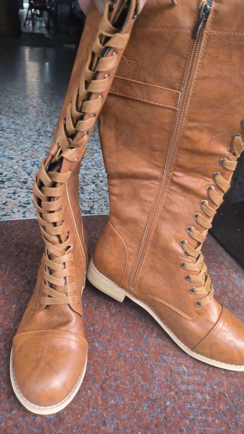 Women's black knee-high knight boots with a cross strap detail across the ankle.