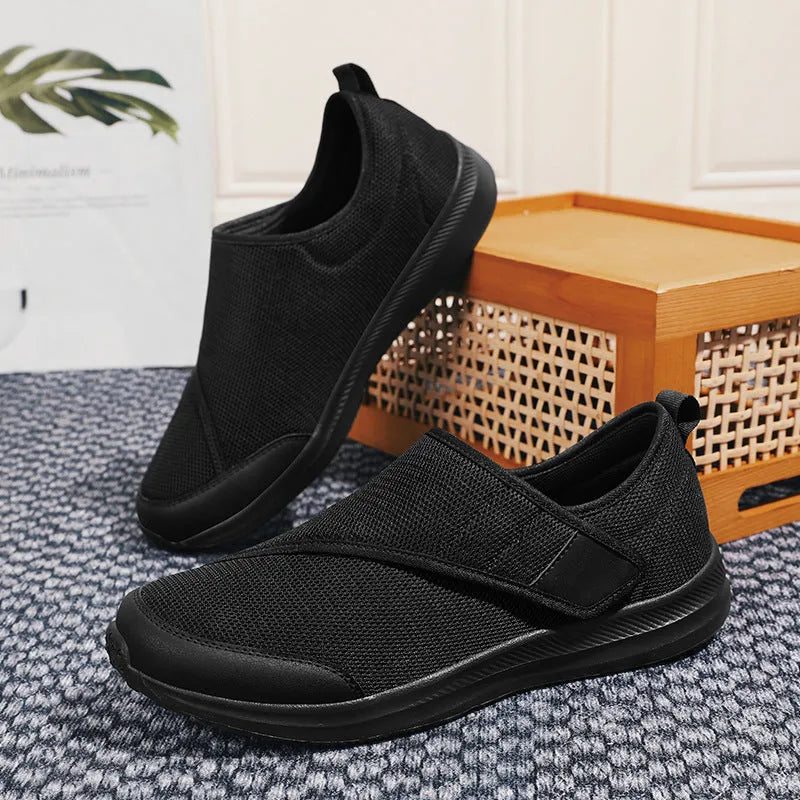 A pair of grey Velcro walking shoes with a mesh upper and round toe, shown on a white background.