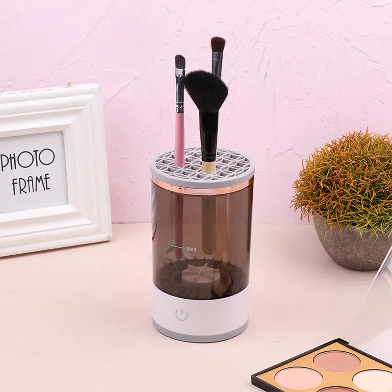 Grey and white electric makeup brush cleaner with USB charging cable on a wooden surface