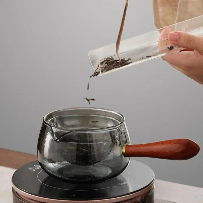 Transparent rotary glass teapot with wooden handle and built-in infuser on countertop