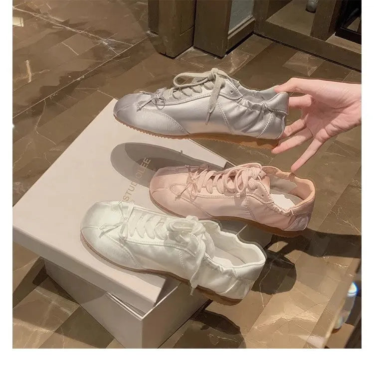 Women's silver grey satin ballet flats with round toe and white lace-up front on a plain background.