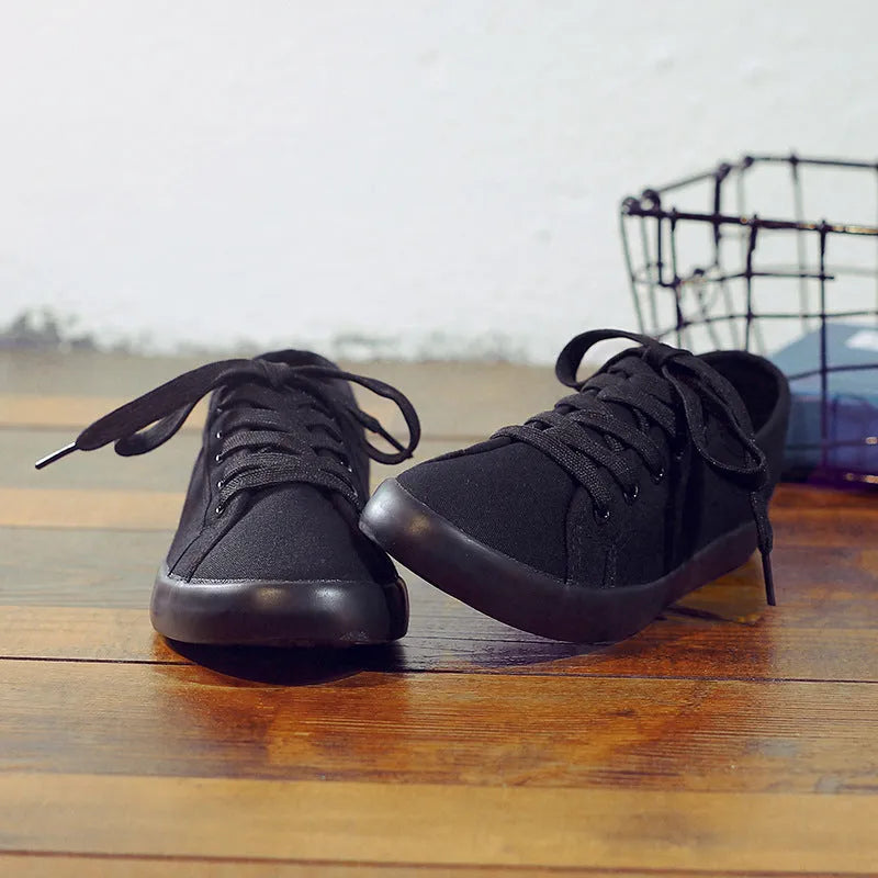 All-black low-top women's canvas shoes with flat rubber sole and lace-up front
