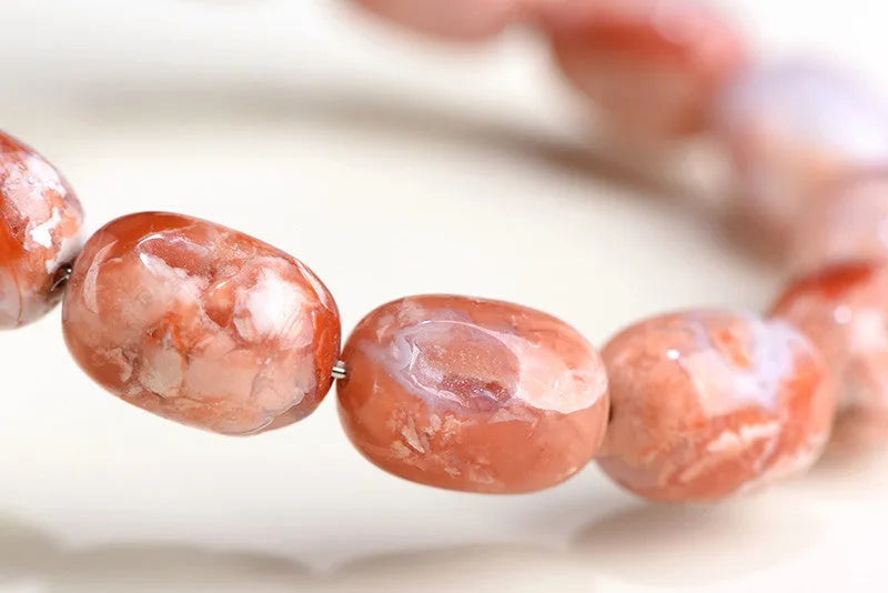 Natural cherry agate barrel bead bracelet with Ruyi charm on a white background.