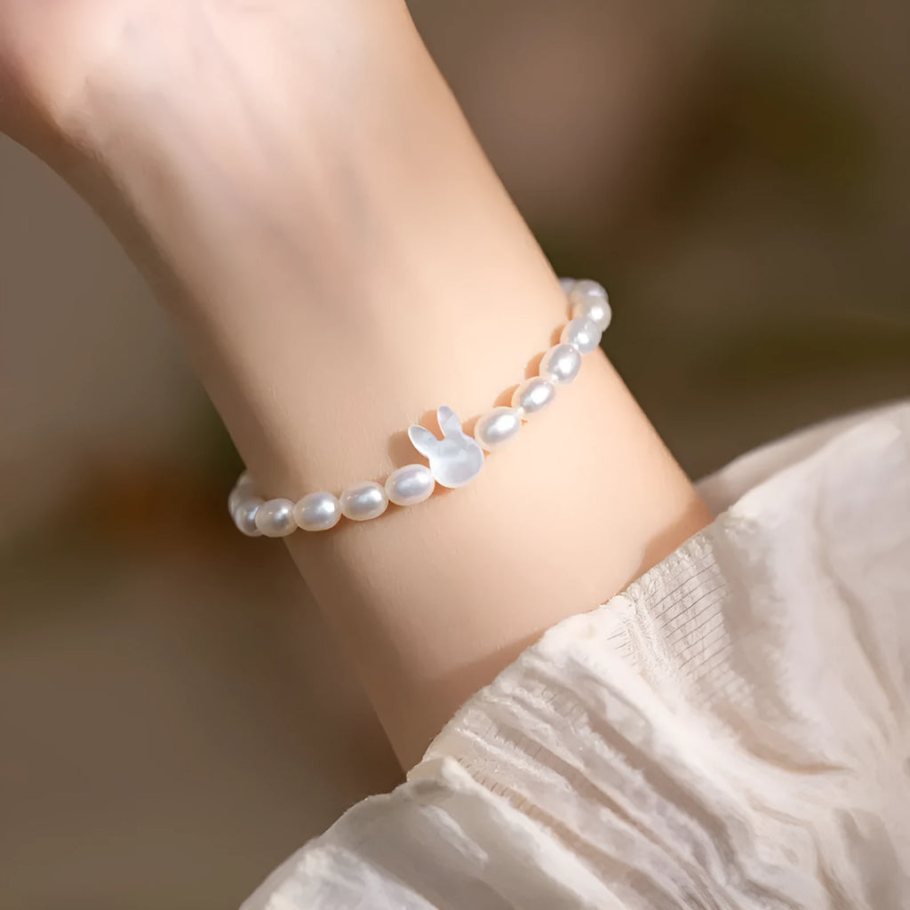 White pearl and 925 silver rabbit charm bracelet on a model's wrist, showing adjustable elastic string.