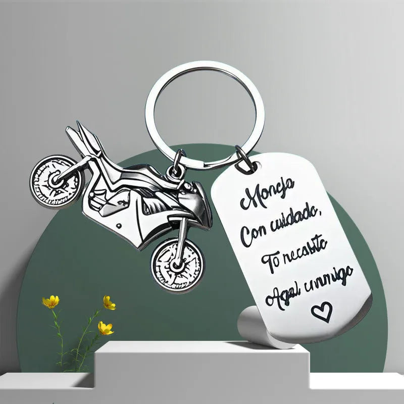 Stainless steel motivational motorcycle keychain with flannel storage pouch on a grey background.