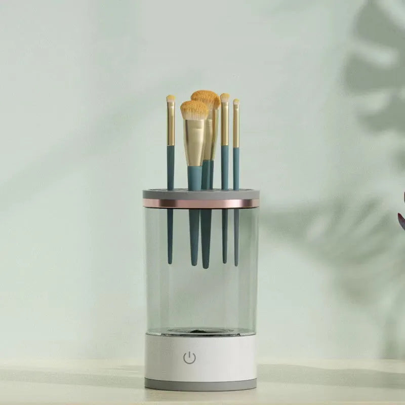Grey and white electric makeup brush cleaner with USB charging cable on a wooden surface