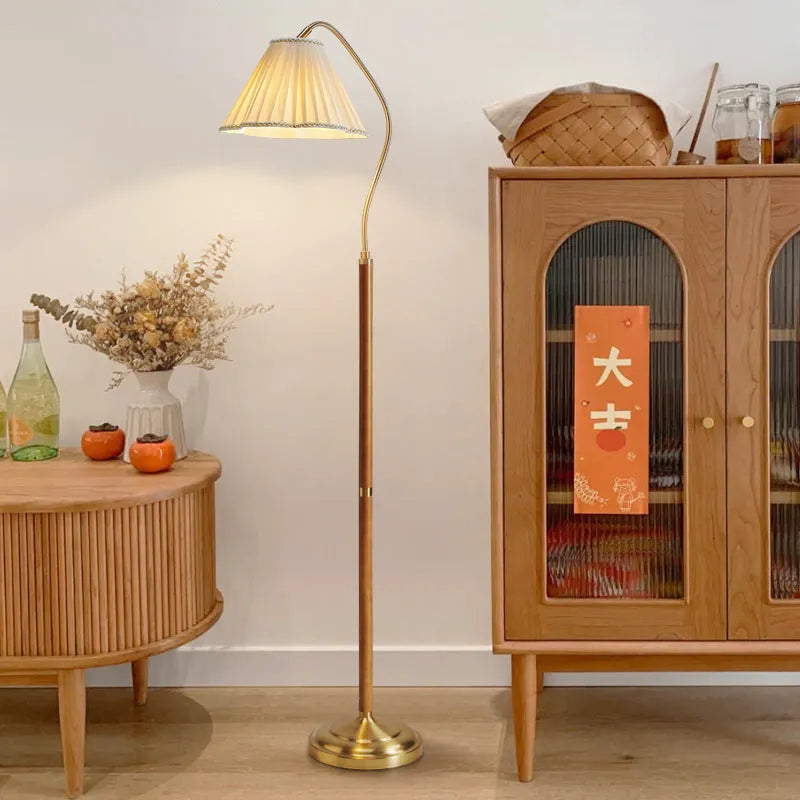 Solid wood floor lamp with fabric shade in walnut colour placed beside a sofa in a living room