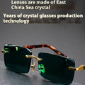 Dark green crystal frameless sunglasses with a case and cleaning cloth on a table.