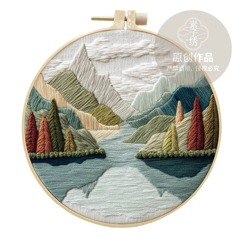 Complete DIY embroidery kit showing pre-printed landscape fabric, coloured threads, needles, and an embroidery frame.