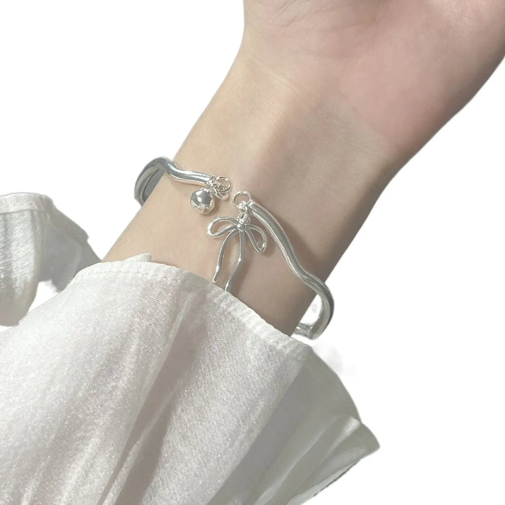 Silver adjustable bow bracelet with a bell opening clasp on a wrist.