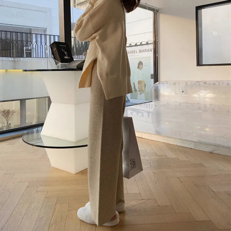 Woman wearing high-waist cream knitted wide-leg trousers with a floor-length, straight-leg silhouette.