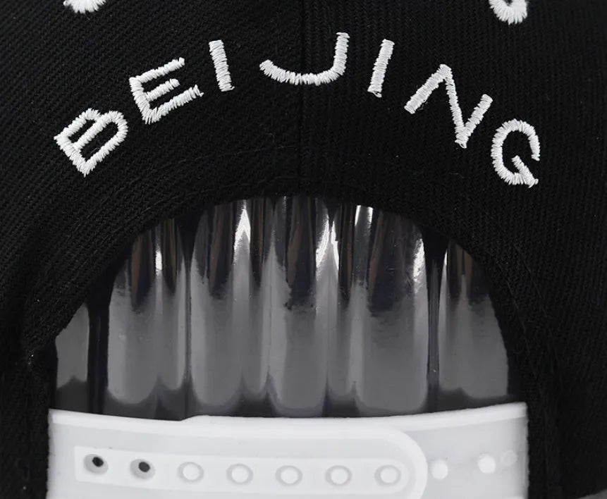 Black and white cotton baseball cap with letter embroidery on the front, showing adjustable strap at back.