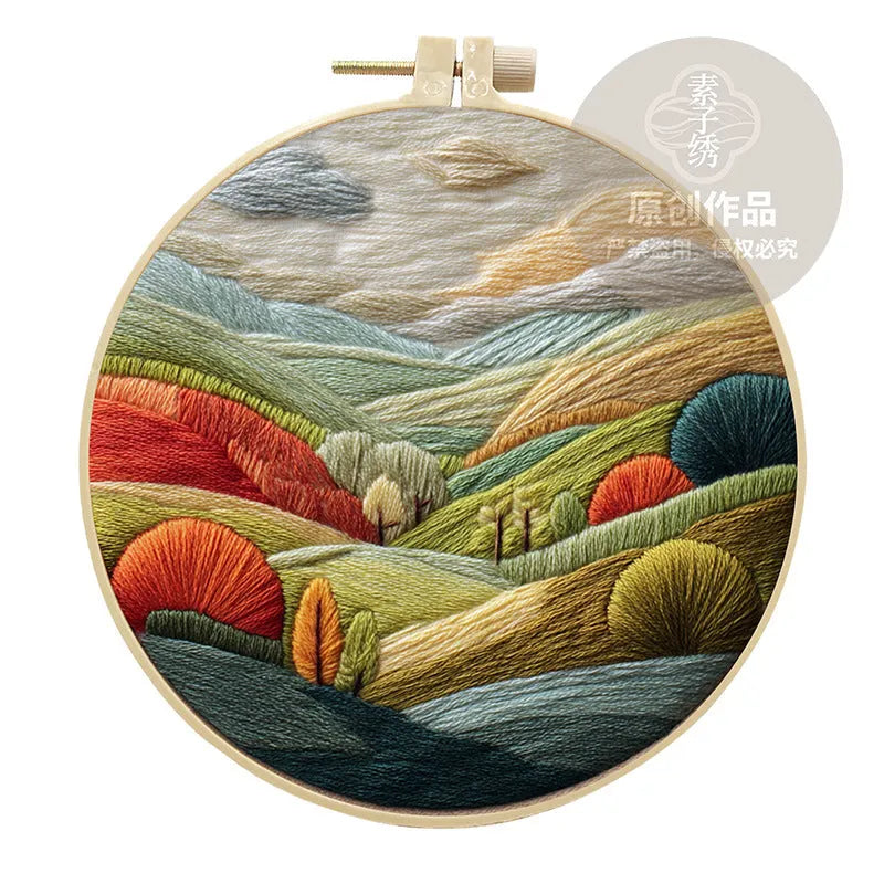 Complete DIY embroidery kit showing pre-printed landscape fabric, coloured threads, needles, and an embroidery frame.