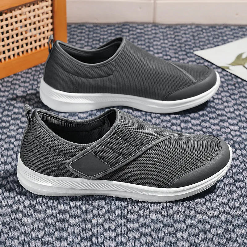 A pair of grey Velcro walking shoes with a mesh upper and round toe, shown on a white background.